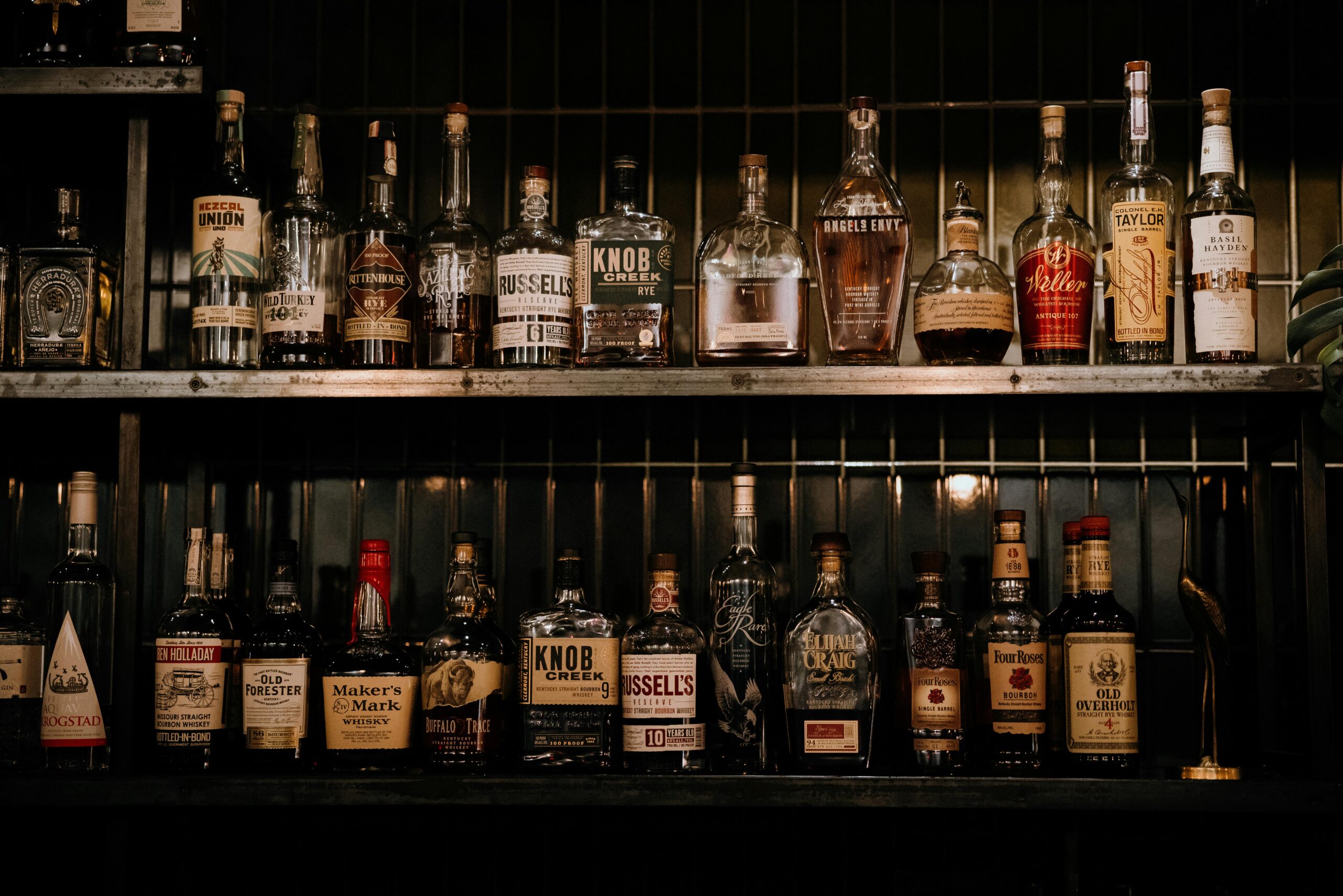 A variety of liquor bottles arranged on shelves in a dimly lit bar setting.
